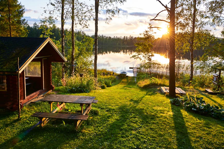 The sun shines on a wooden cabin at the edge of a lake in Finland