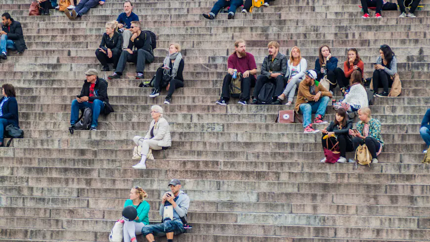 People sit on stairs on the Senate Square in front of the Finnish Evangelical Lutheran cathedral in Helsinki, FInland