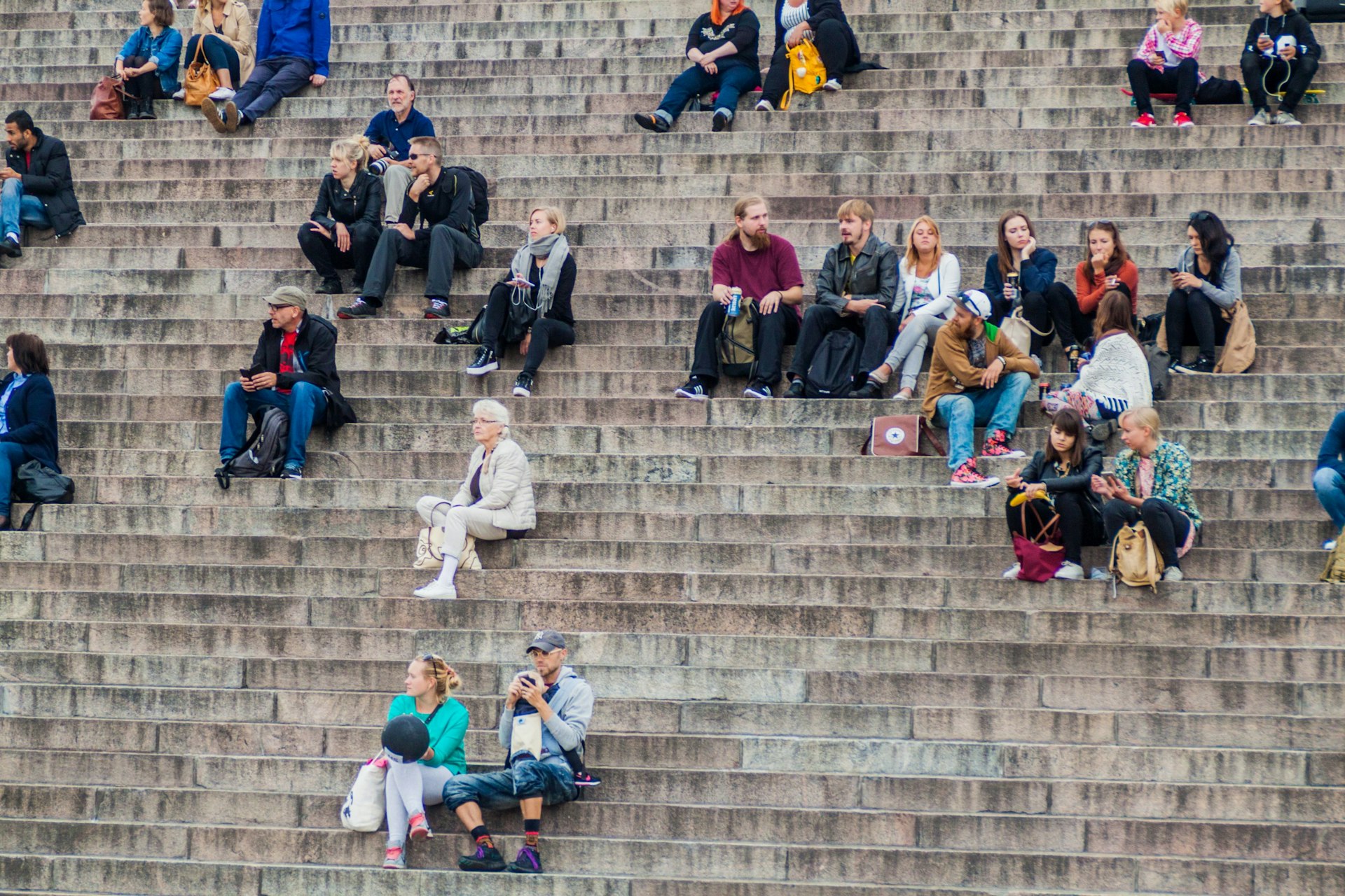 People sit on stairs on the Senate Square in front of the Finnish Evangelical Lutheran cathedral in Helsinki, FInland
