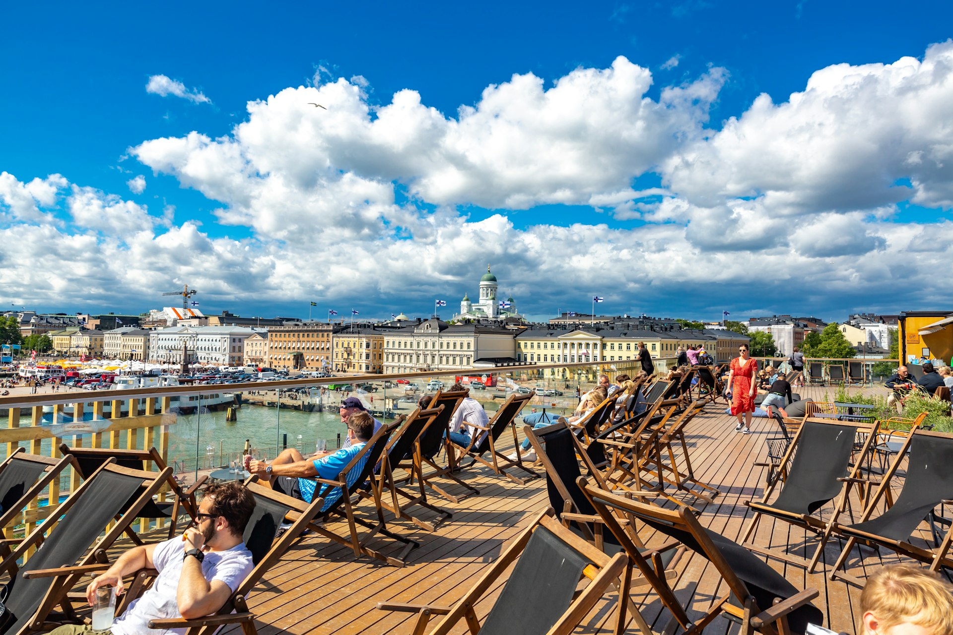 People lounge in the sun on some decking by the water in Helsinki