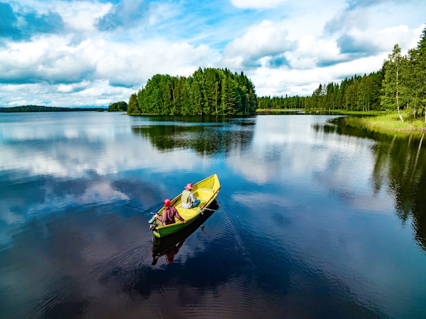 Aerial view of fishing boat with young woman and man in blue summer lake in Finland; Shutterstock ID 1950372253; your: Claire Naylor; gl: 65050; netsuite: Online ed; full: Finland best places