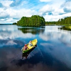 Aerial view of fishing boat with young woman and man in blue summer lake in Finland; Shutterstock ID 1950372253; your: Claire Naylor; gl: 65050; netsuite: Online ed; full: Finland best places