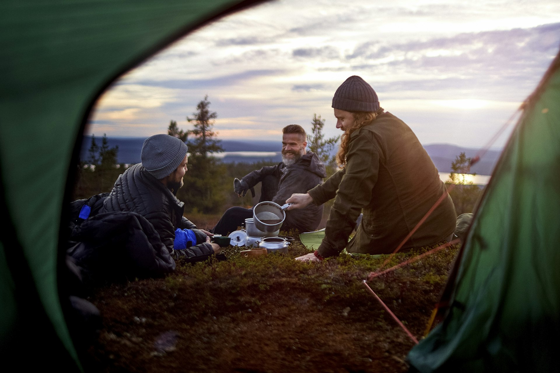 Three male hikers prepare a meal in front of tent in Lapland, Finland