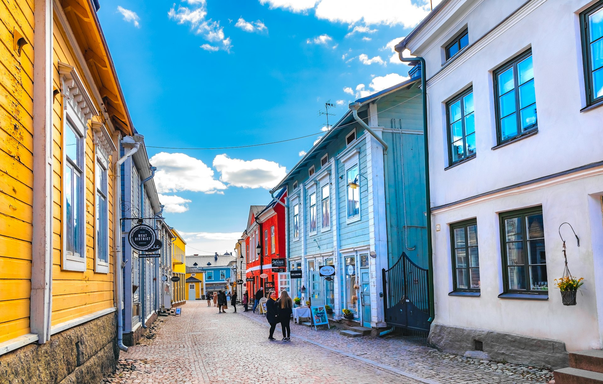 A street perspective with people walking by colorful wooden houses under a bright blue sky in Porvoo, Finland, Europe