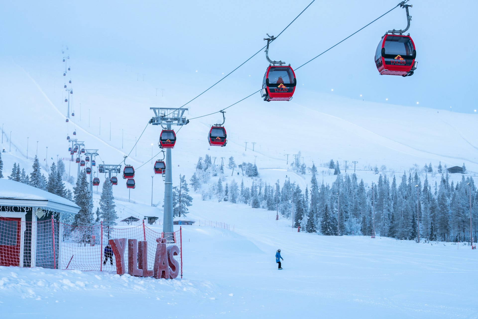 A series of red gondolas travel along a wire leading up a ski slope covered in snow in Yllas, Finland