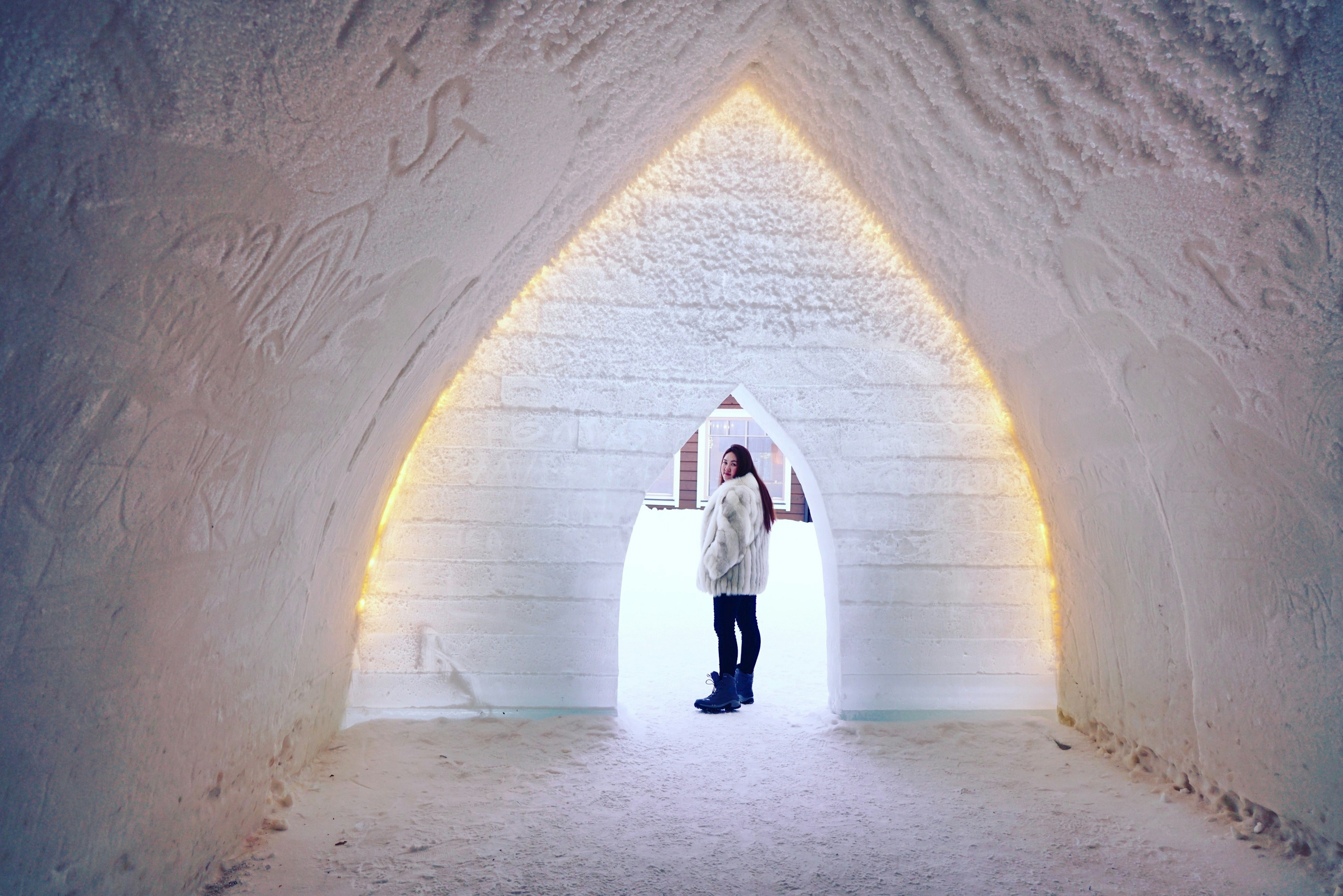 A woman in snow gear looks back through an archway carved in ice in a snow castle in Finland