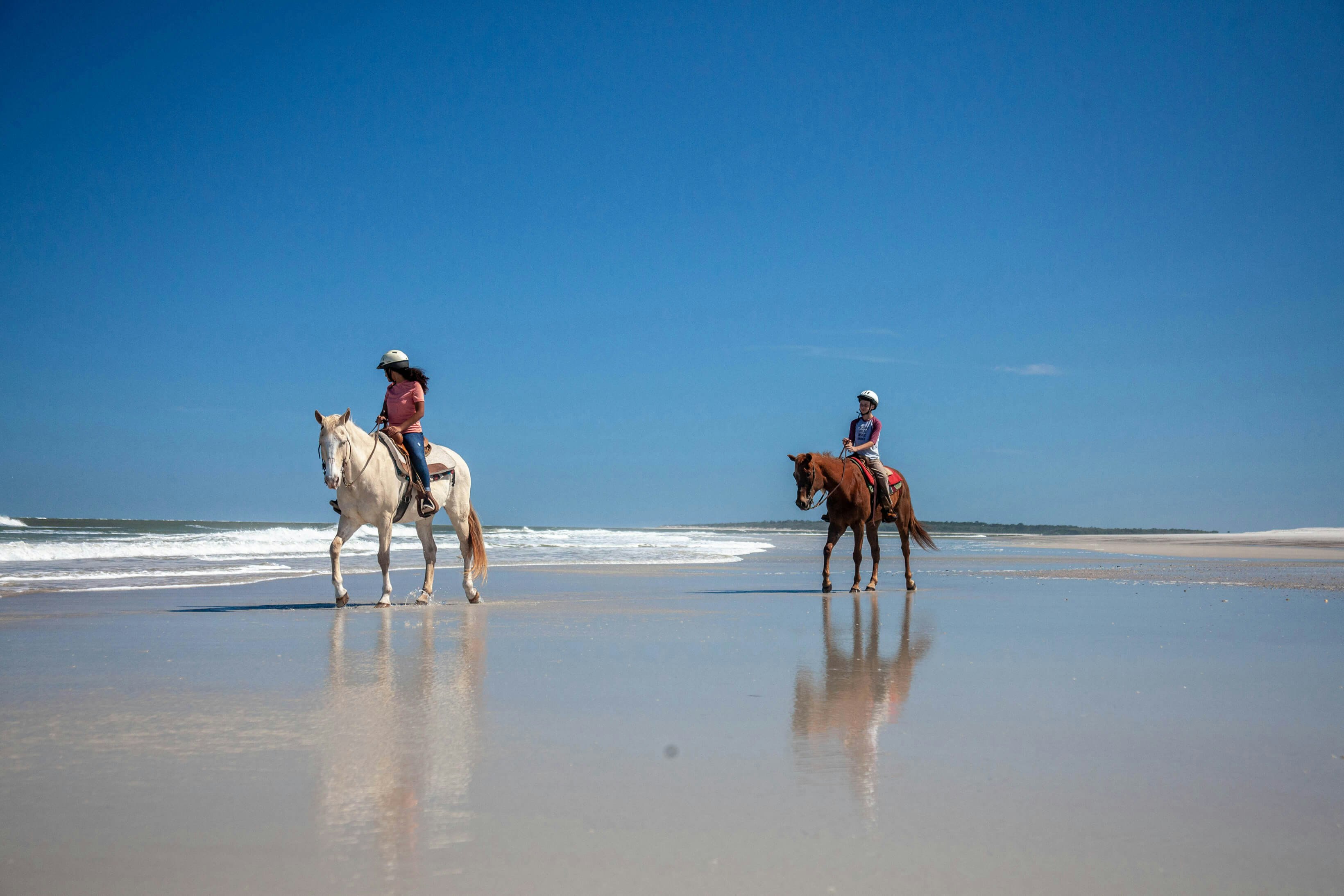 Two people horseback riding on an empty beach on Amelia Island, Florida, on a clear sunny day