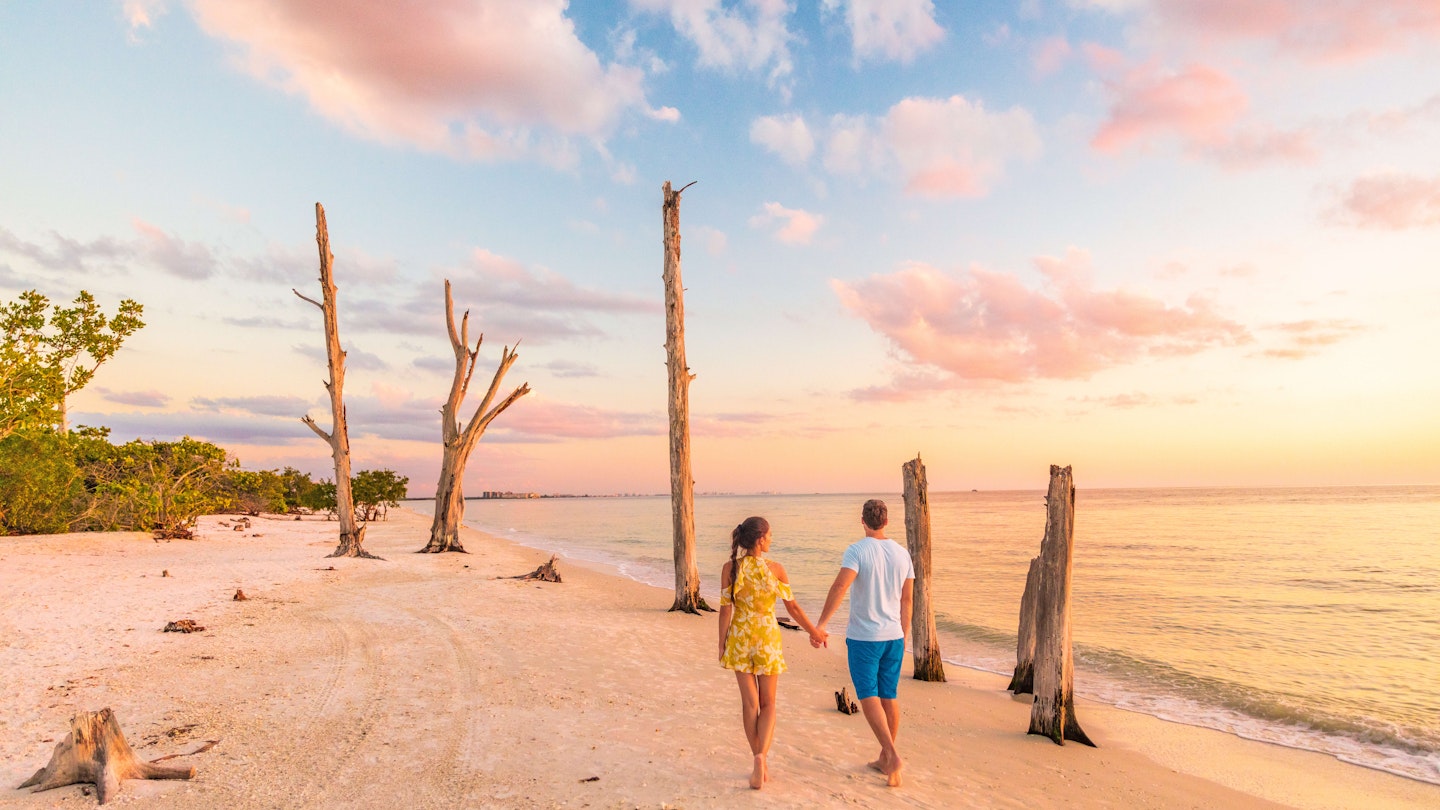 Couple walking on beach at sunset romantic travel getaway, idyllic Florida destination, Lovers Key State Park in the gulf of Mexico. Woman and man holding hands relaxing. Southwest Florida.