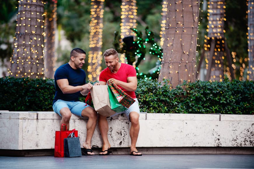 Un couple gay avec des sacs à provisions, assis dehors et regardant leurs achats