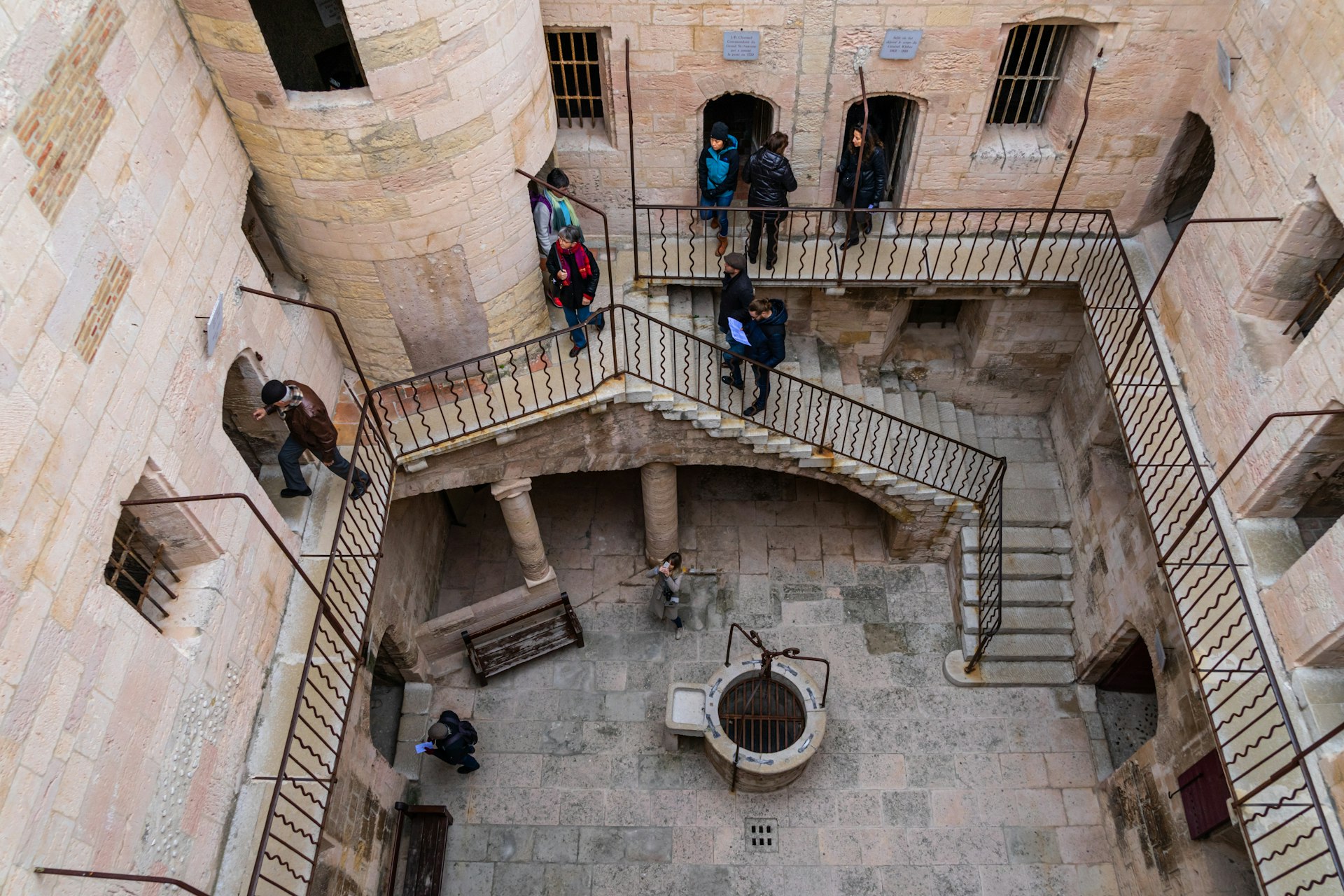 A series of stairs in an old fort and prison building viewed from above as tourists make their way around