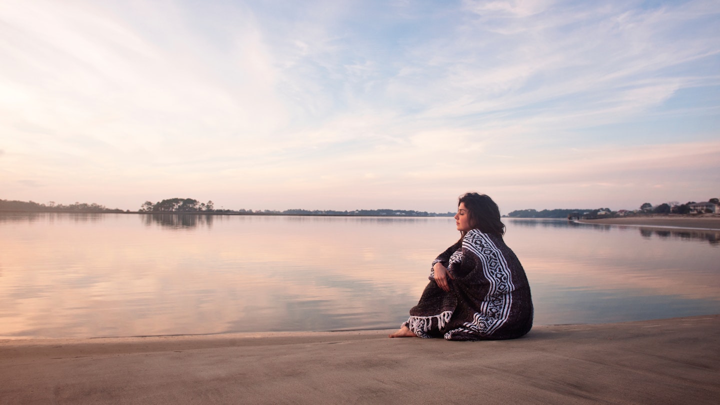 Young woman wrapped in a blanket sitting on a sandbar in Georgia, USA