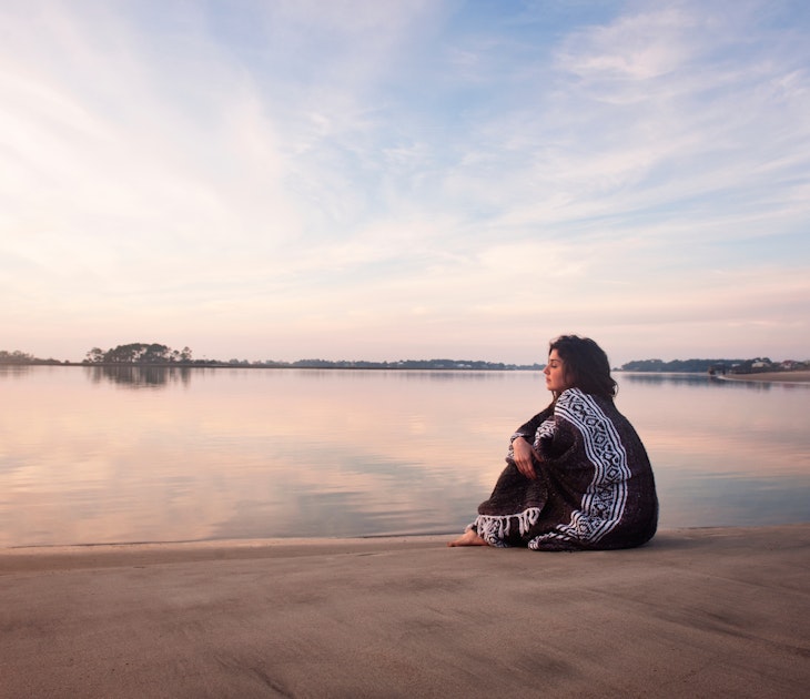 Young woman wrapped in a blanket sitting on a sandbar in Georgia, USA