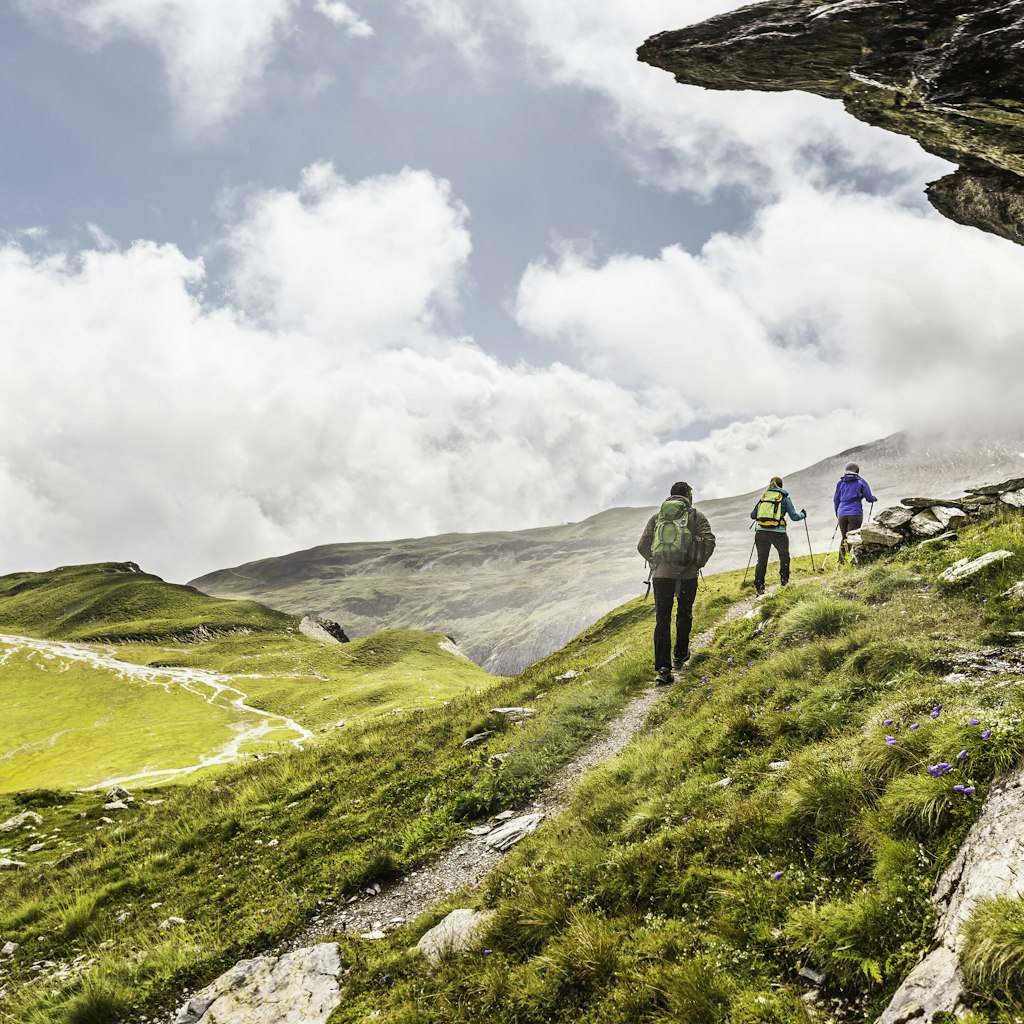 Rear view of three hikers hiking beneath rock overhang, Fil de Cassons, Segnesboden, Graubunden, Switzerland