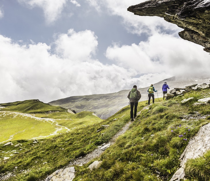Rear view of three hikers hiking beneath rock overhang, Fil de Cassons, Segnesboden, Graubunden, Switzerland