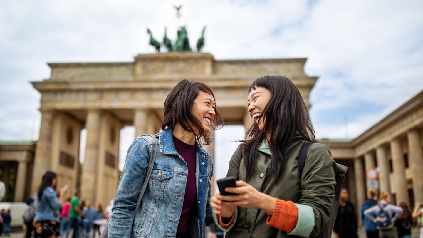 Cheerful female friends standing against Brandenburg Gate in city during vacation
