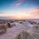 Beachscape of classic English coast at dusk with beach, marram grass, fence line.