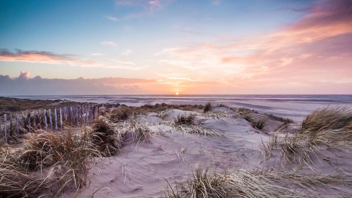 Beachscape of classic English coast at dusk with beach, marram grass, fence line.