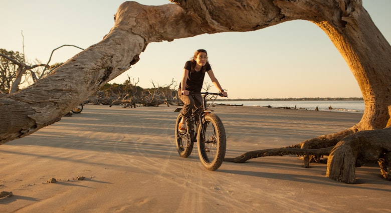 Woman riding her fatbike along a beach on the ocean.