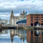 Albert Dock in Liverpool, with surrounding buildings and boats reflected in the water, and with the Royal Liver Building in the background.