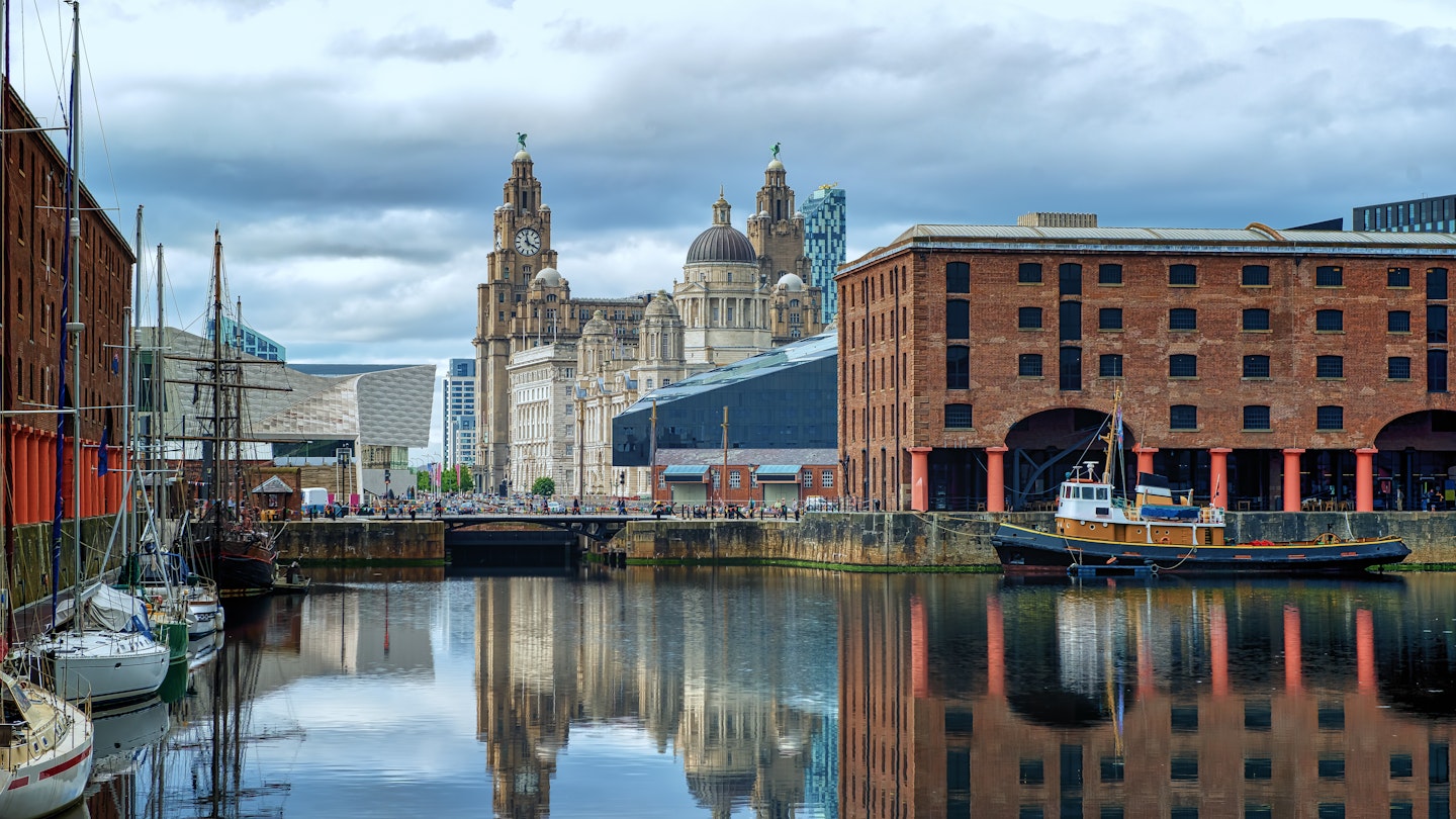 Albert Dock in Liverpool, with surrounding buildings and boats reflected in the water, and with the Royal Liver Building in the background.