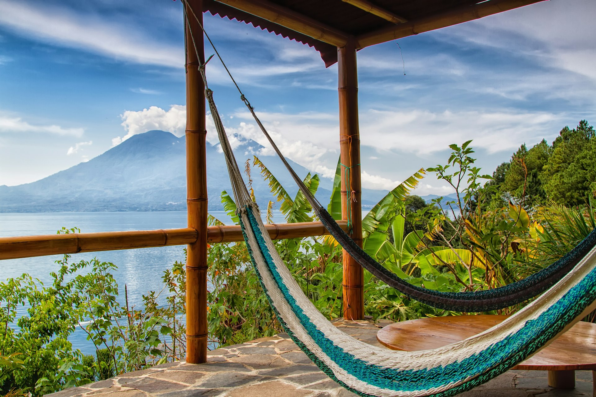 Two hammocks strung up on a cabin balcony overlooking a lake and volcano in Guatemala