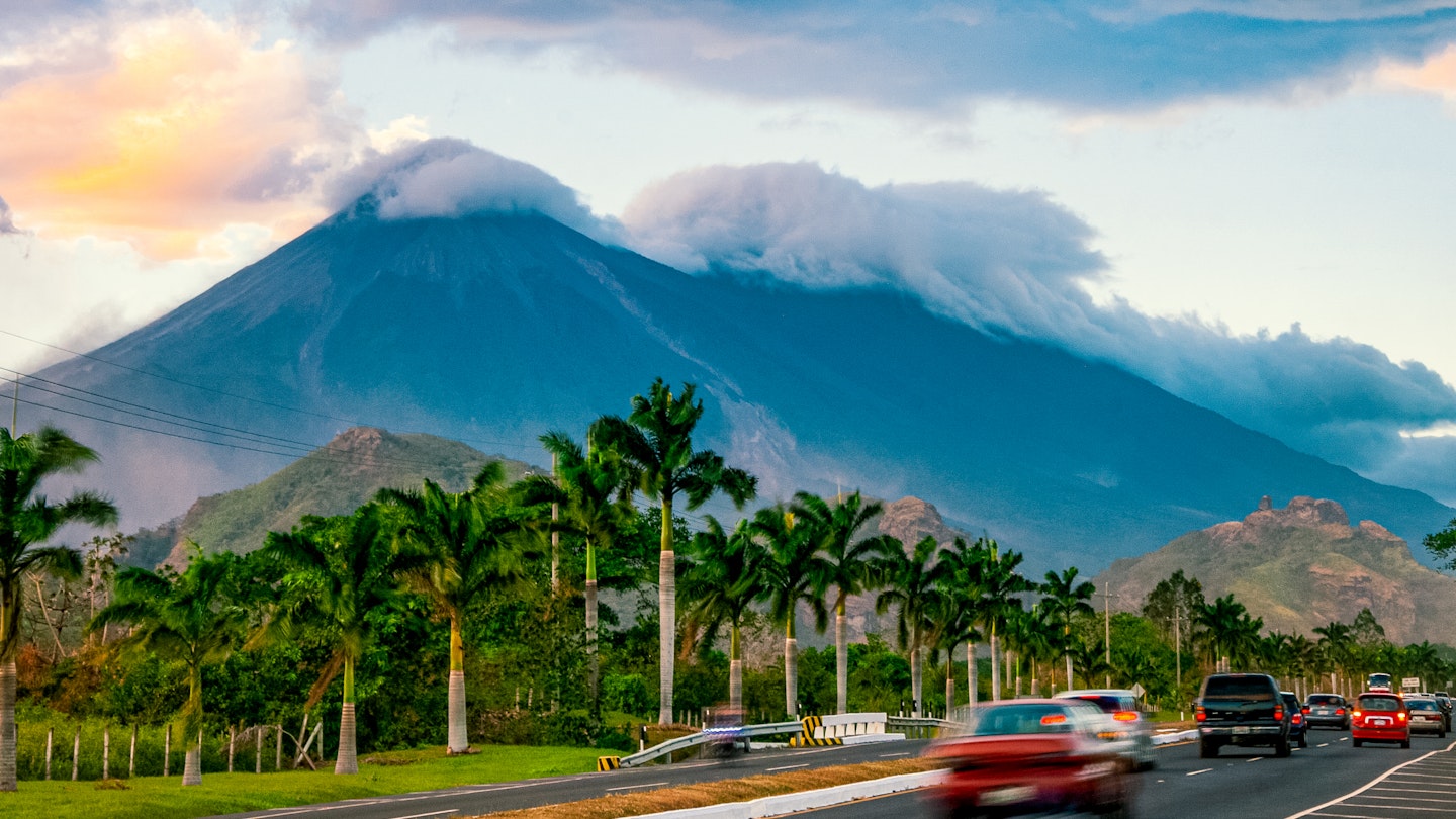Cars drive past Volcanoes Fuego y Acatenango in Palin, Guatemala, at sunset