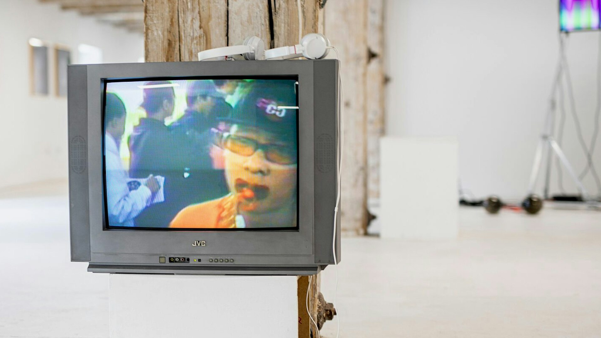 Installation view of a television with a person on the screen and headphones on top, Techno Worlds, Budapest
