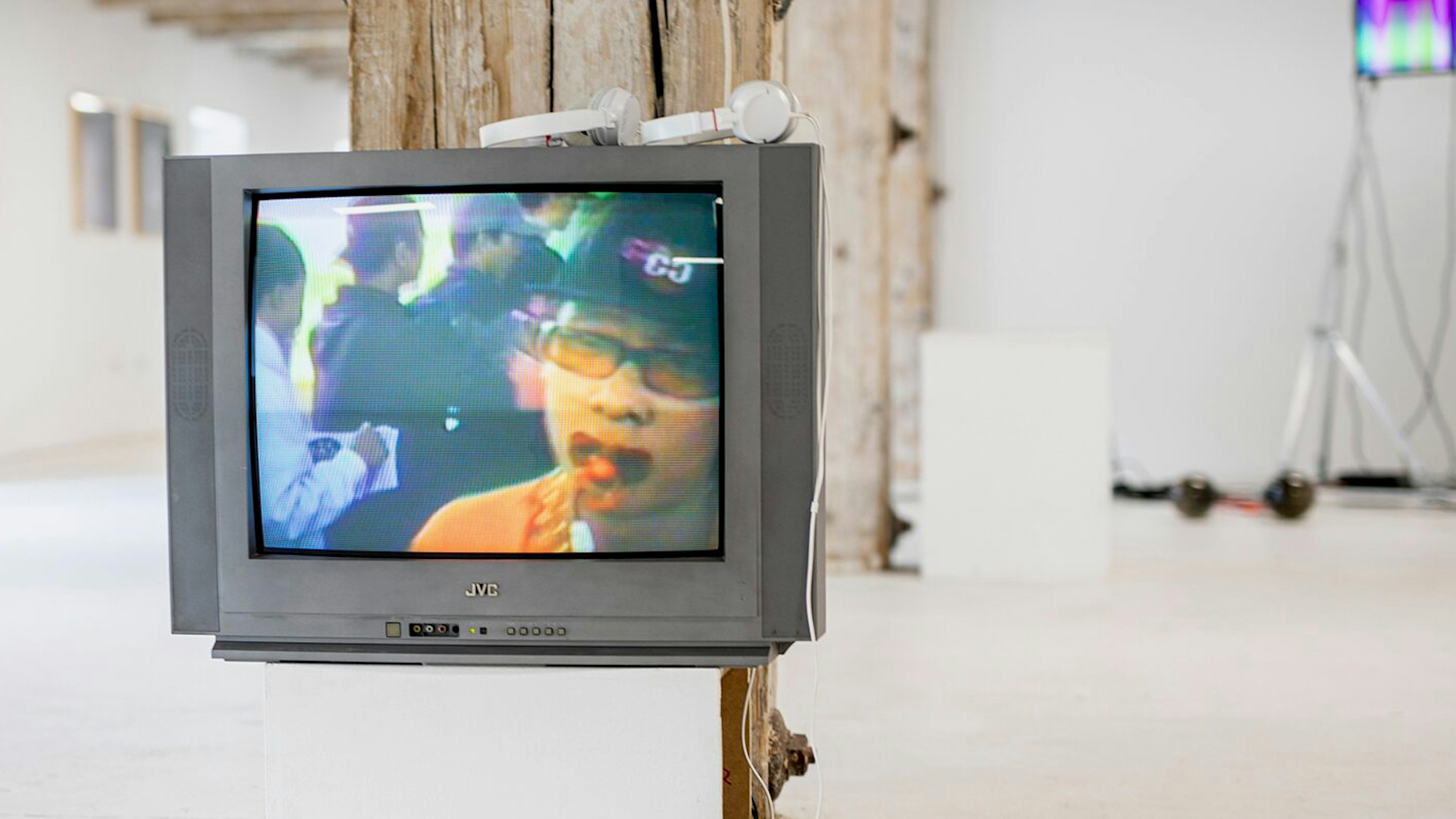 Installation view of a television with a person on the screen and headphones on top, Techno Worlds, Budapest