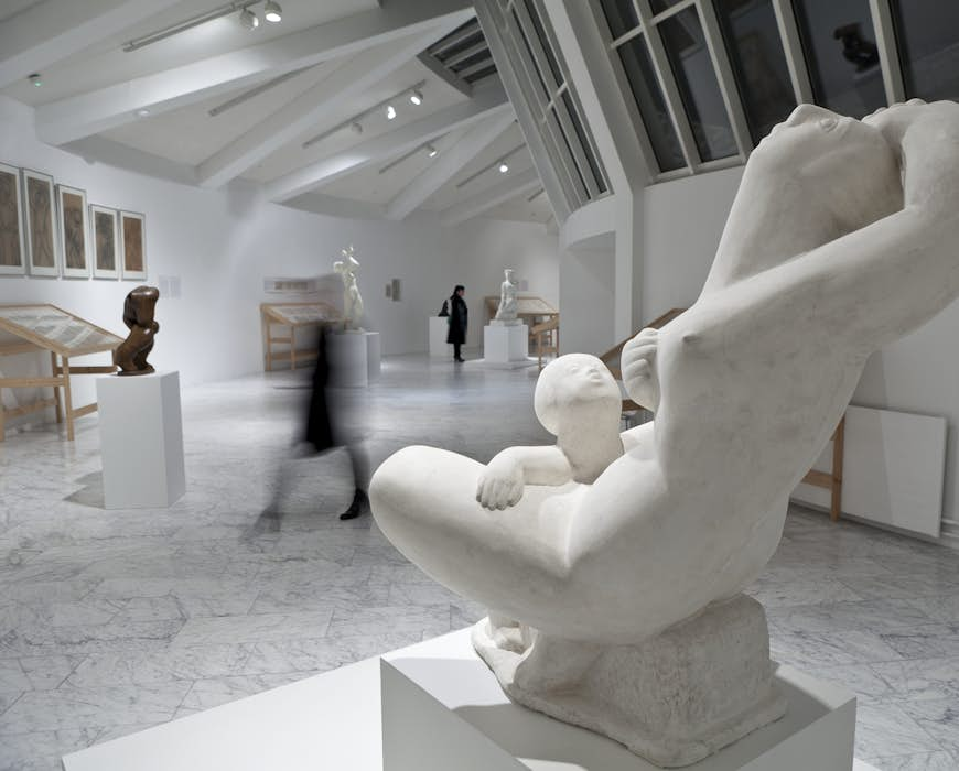 A person blurred by the camera walks through a white art hall past a sculpture made by Asmundur Sveinsson. Reykjavik Iceland