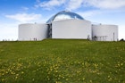 The Perlan museum sits on a green hill, identifiable by four large water tanks sitting around a central reflective dome. Reykjavik.
