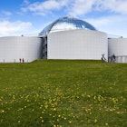 The Perlan museum sits on a green hill, identifiable by four large water tanks sitting around a central reflective dome. Reykjavik.