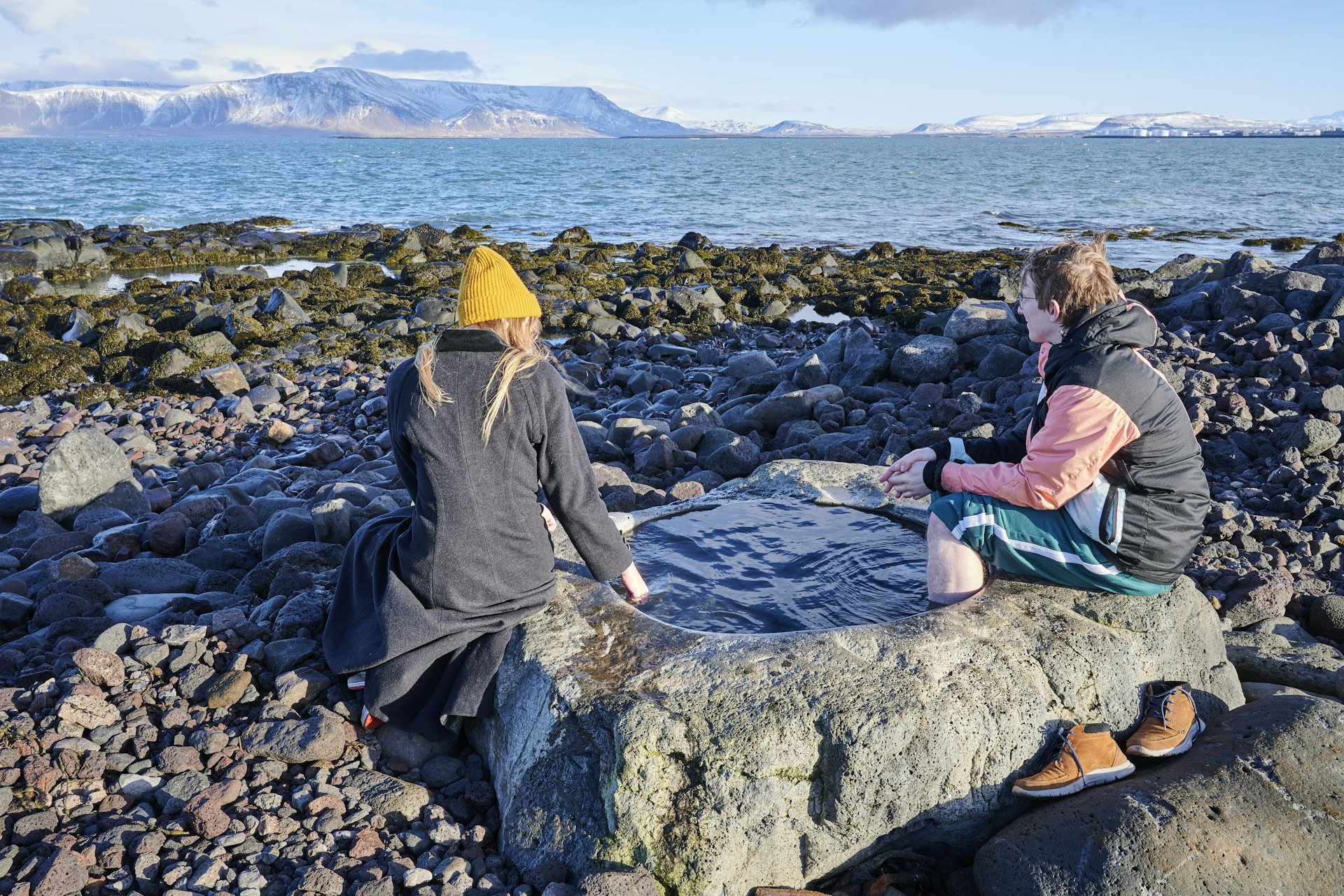 A young couple enjoys the hot water of the Kvika Footbath overlooking Greenland Sea in Seltjarnarnes.