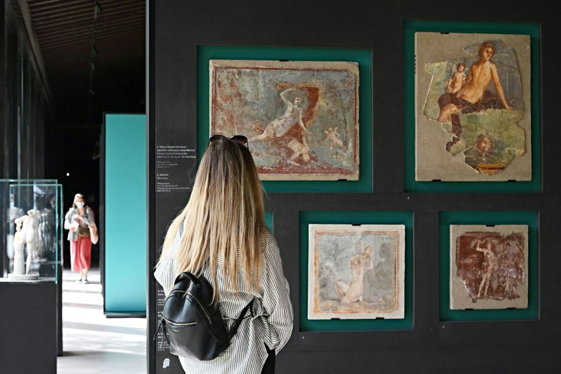 A blonde woman looks at old erotic frescoes displayed against a green wall which form part of a new exhibition in Pompeii called "Art and sensuality in the houses of Pompeii"