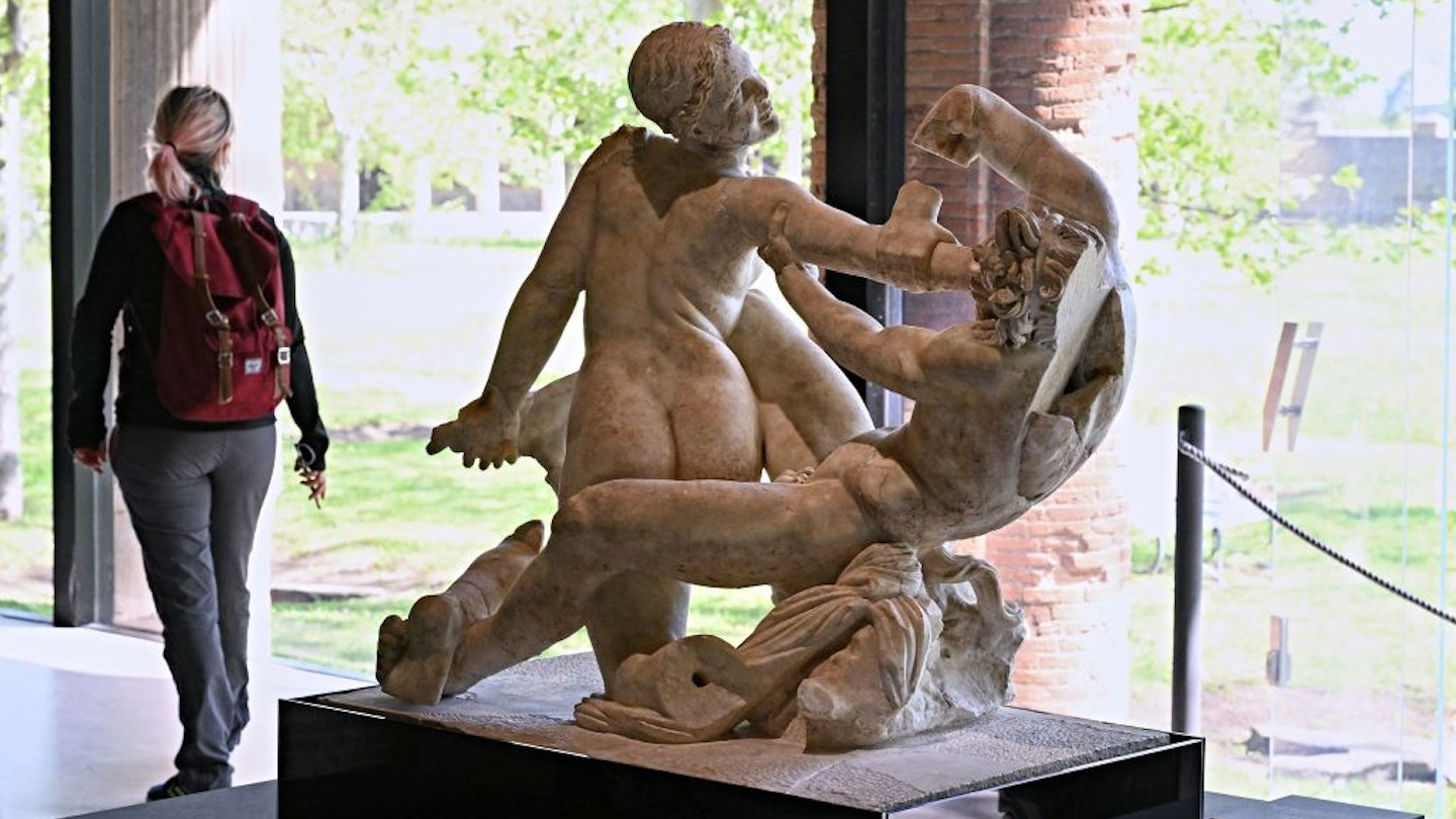 A vistor walks next to a "Satyr and hermaphrodite" sculpture, in Pompeii's site of a new exhibition entitled "Art and sensuality in the houses of Pompeii" on art and sexuality in the ancient city, where sculptures and paintings of breasts and buttocks abounded, on April 28, 2022. - Raunchy scenes may redden faces at a new exhibition in Pompeii on art and sexuality in the ancient Roman city, where sculptures and paintings of breasts and buttocks abounded. Archaeologists excavating the city, which was destroyed by the eruption of nearby Vesuvius in 79 AD, were initially startled to discover erotic images everywhere, from garden statues to ceiling frescos. (Photo by Andreas SOLARO / AFP) (Photo by ANDREAS SOLARO/AFP via Getty Images)