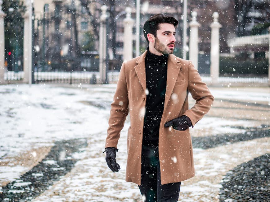 Красивый молодой человек, стоящий на улице зимой, в заснеженном городе Турин, Италия, в кремовом пальто