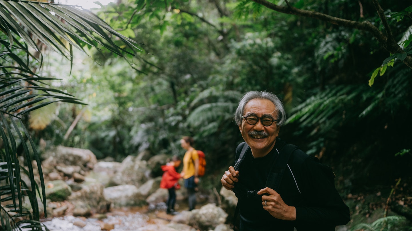 Active senior Japanese man enjoying hiking through river in rainforest, Iriomote-Ishigaki National Park, Okinawa, Japan