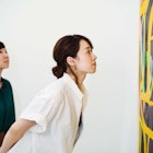 Two women standing in an art gallery, looking at an abstract modern painting. - stock photo