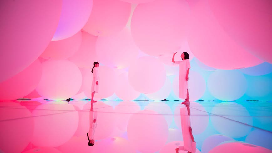 Neon-pink artwork featuring two people in white in a mirrored room filled with hovering globes or balloons