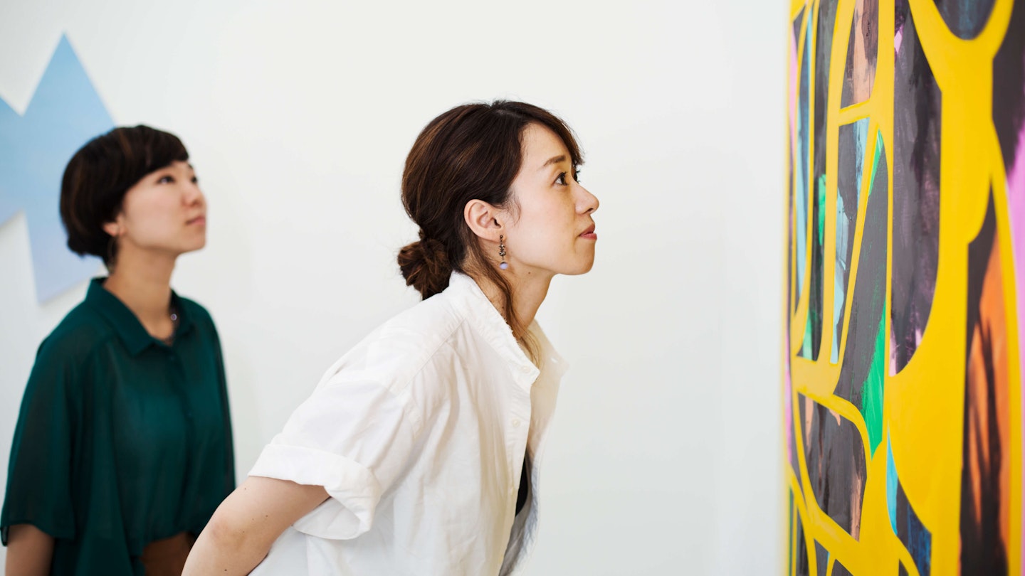 Two women standing in an art gallery, looking at an abstract modern painting. - stock photo