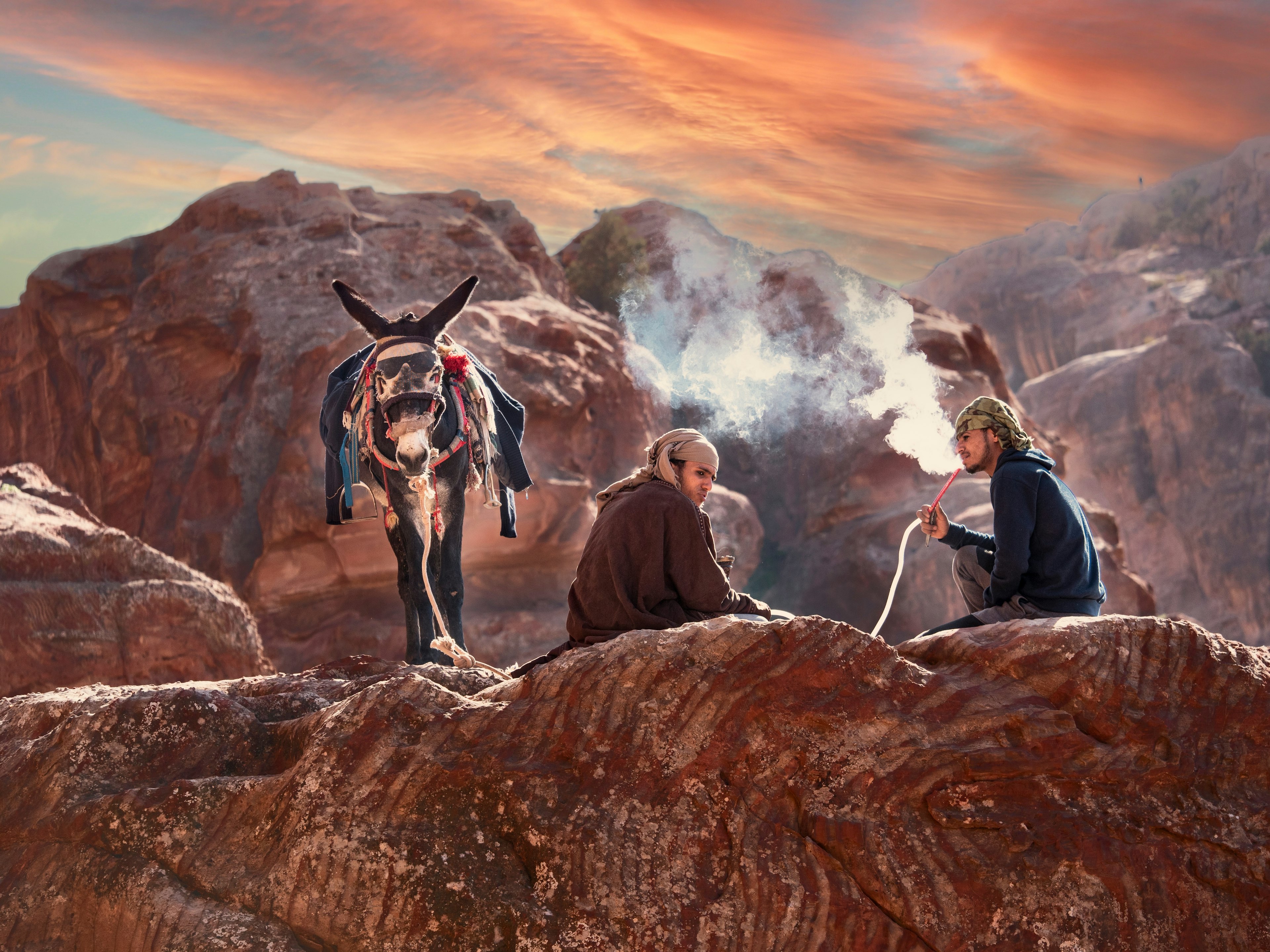 Two young local men smoke shisha next to their donkey in Petra, Jordan, Middle East