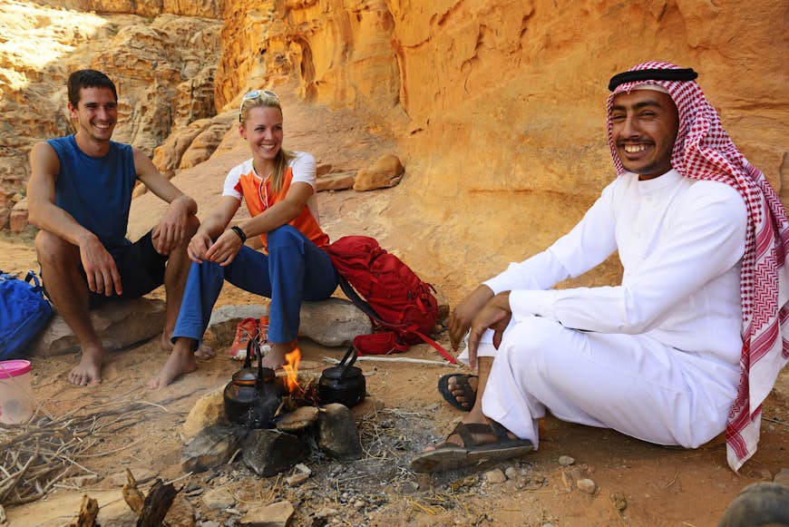 Два улыбающихся туриста пьют чай со своим гидом-бедуином в Вади-Рам, Иордания.