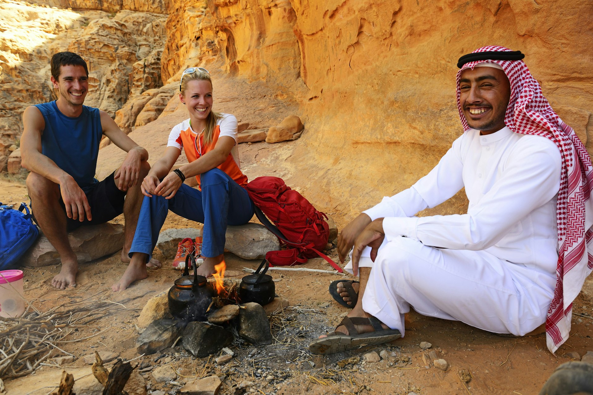 Two tourists smile as they drink tea with their Bedouin guide in Wadi Rum, Jordan