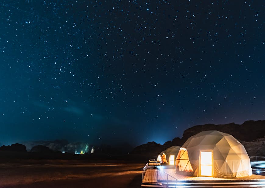 A row of dome-like tents in the desert of Wadi Rum with a nighttime sky full of stars above
