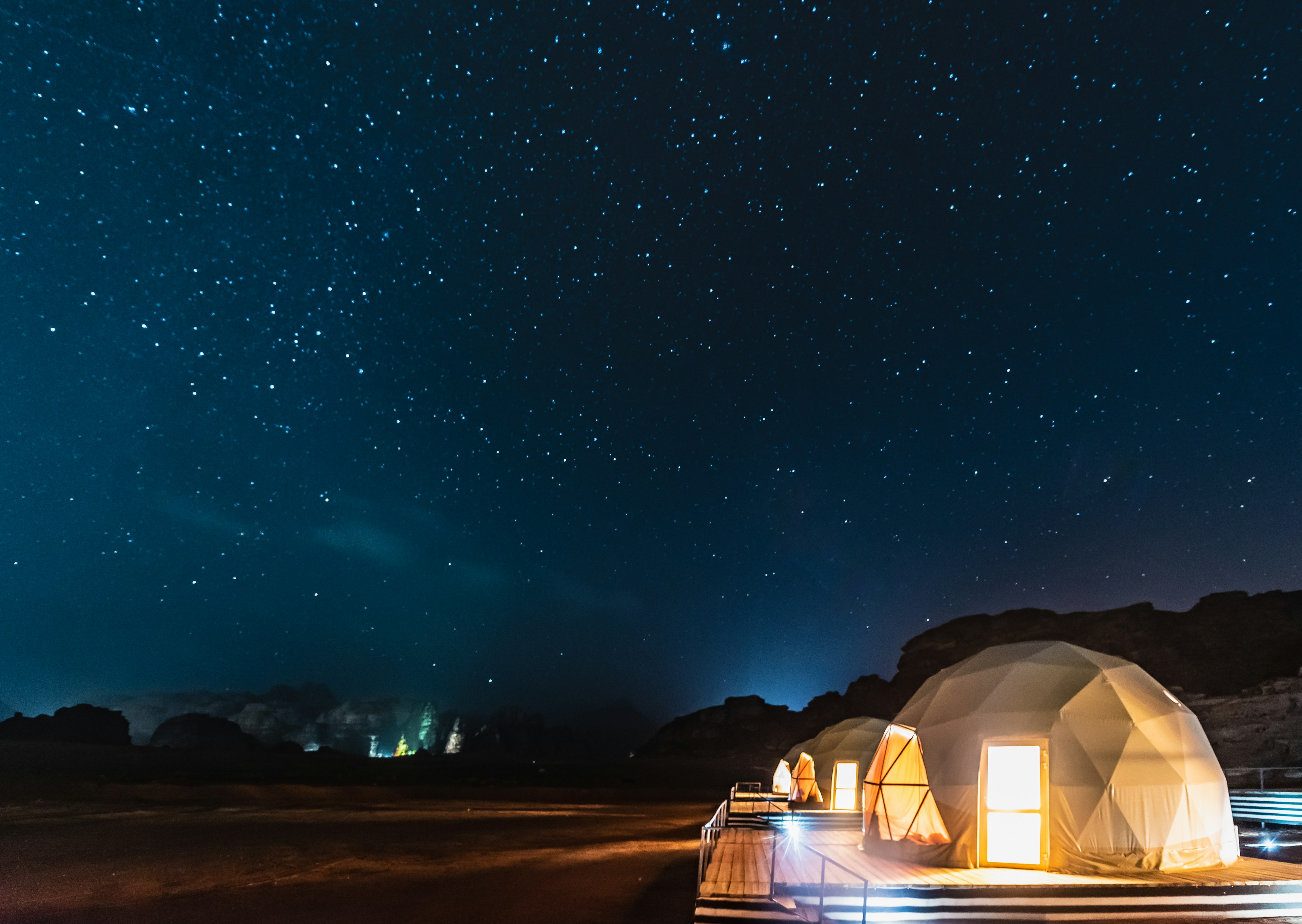 A row of dome-like tents in the desert of Wadi Rum with a nighttime sky full of stars above