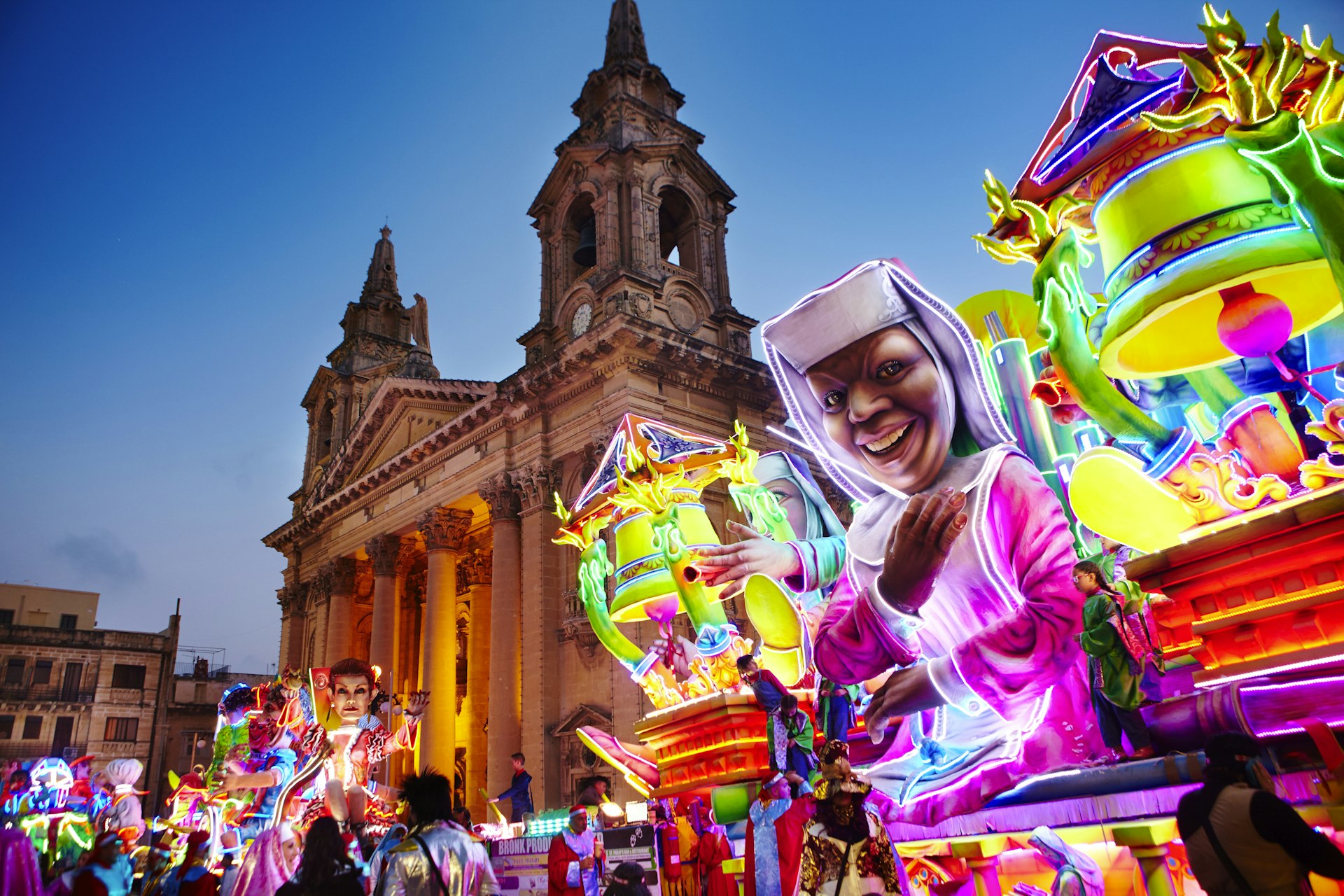 A neon-bright float inspired by the movie Sister Act passes by St Publius Parish Church in Floriana