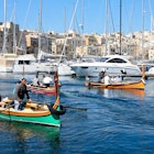 Passengers on traditional Maltese Dghajsa water taxis crossing the harbor at Birgu