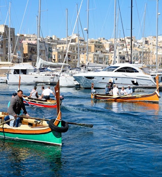 Passengers on traditional Maltese Dghajsa water taxis crossing the harbor at Birgu