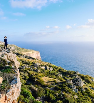 A young woman stands at a height overlooking the Dingli cliffs and the Mediterranean Sea. Her hair is blown by the wind. She seems tiny compared to the majesty of nature.; Shutterstock ID 2116149431; your: Brian Healy; gl: 65050; netsuite: Lonely Planet Online Editorial; full: Best national parks in Malta