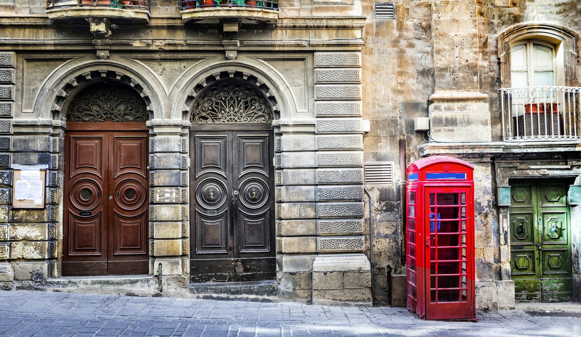 Old streets in Valletta, Malta, with two ornate wooden doors juxtaposed with a bright red phone box.