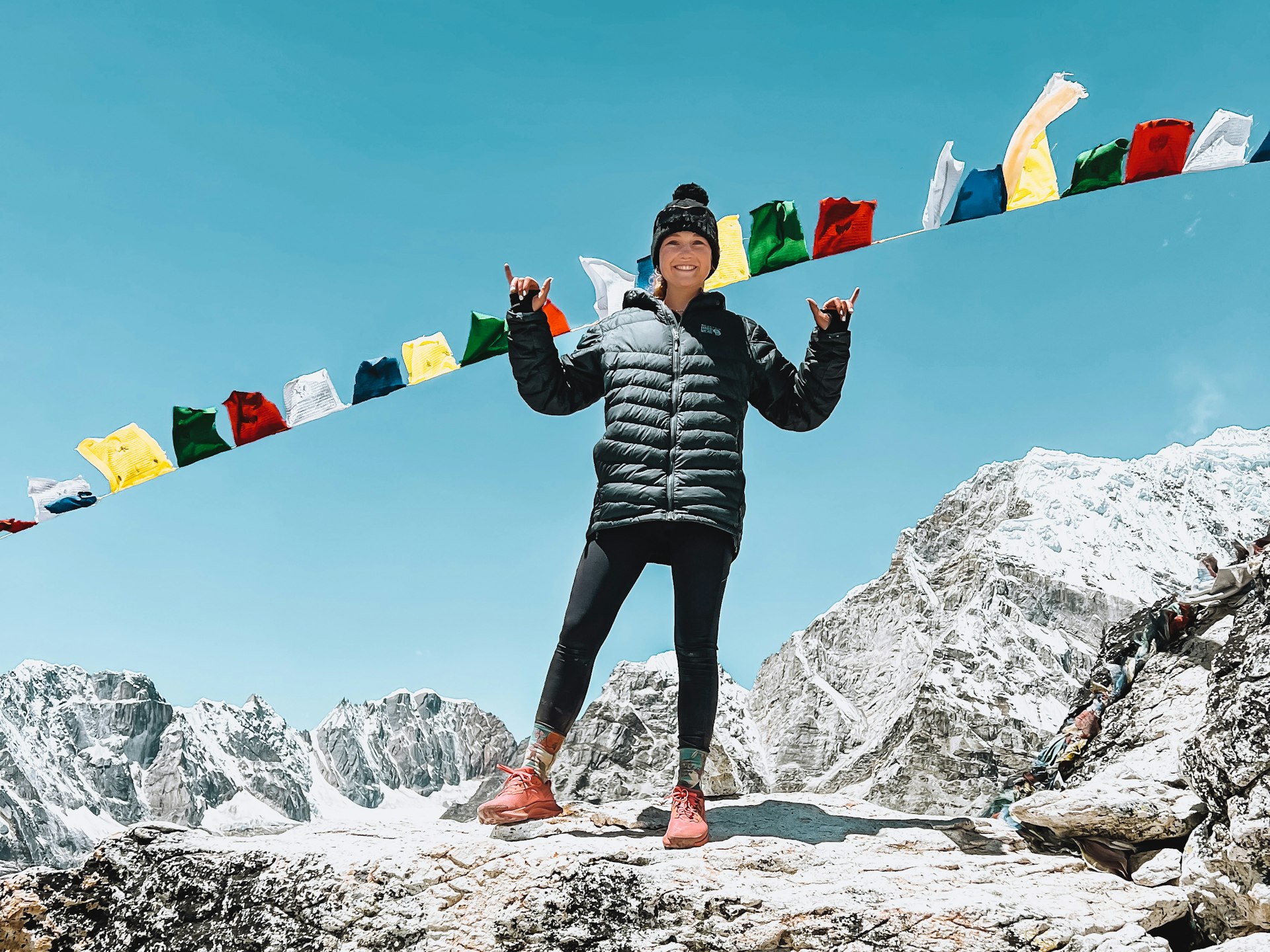 Lucy Westlake at Base Camp, standing on rocky ground under a row of flags